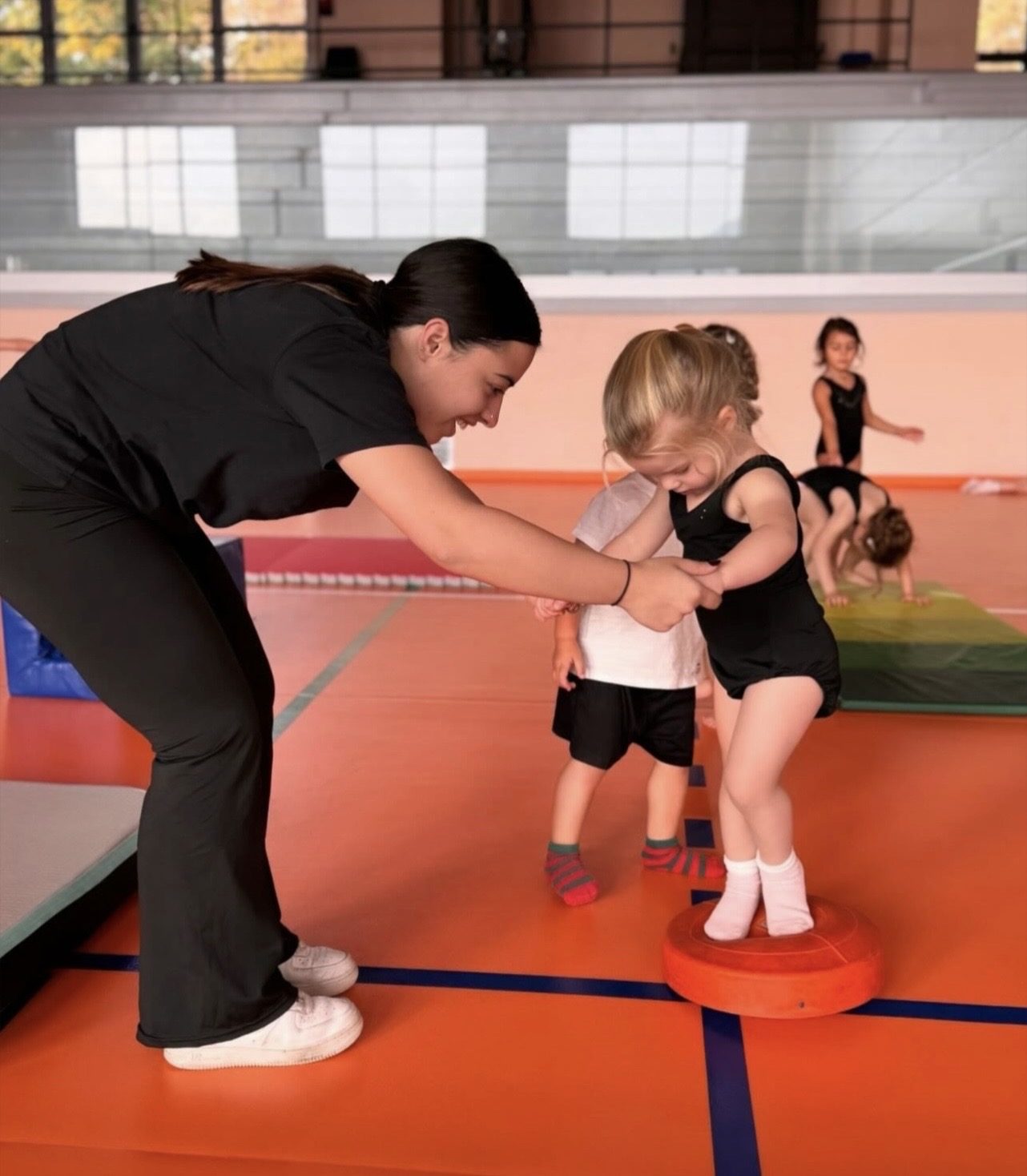 Insegnante aiuta due bambini in equilibrio su un attrezzo durante il corso di Baby Gym