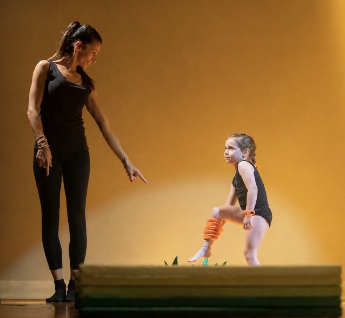 Insegnante segue una bambina in equilibrio su una panca durante la lezione