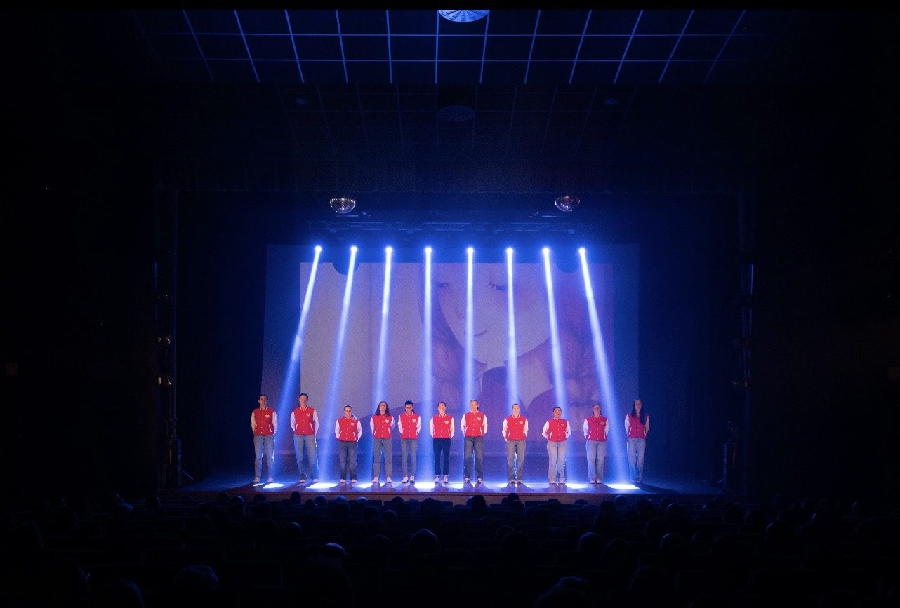 Le insegnanti con la giacca rossa in controluce sul palco del teatro